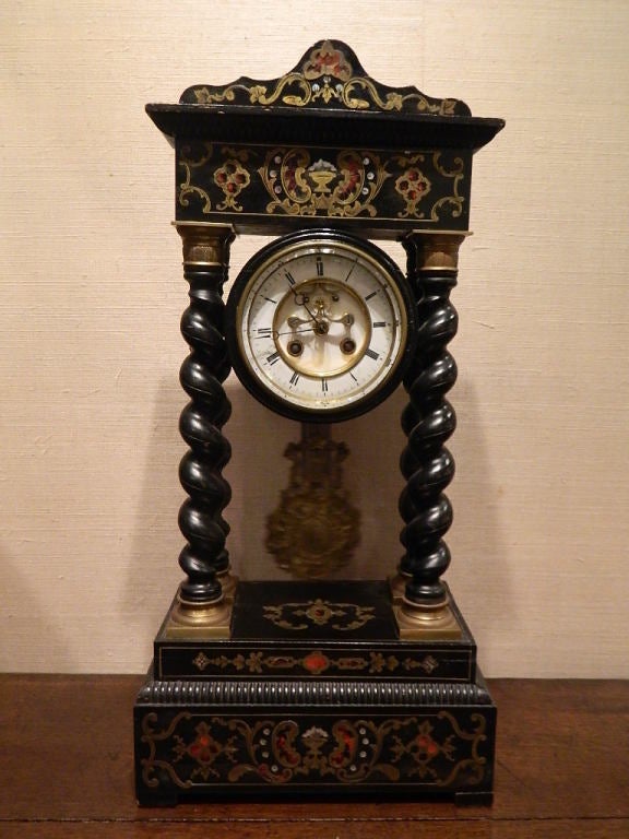 French boulle mantel clock. The clock is enhanced by a beautifully boulle decorated base. The top decorated pediment is sustained by four turned columns. A framed enameled face with Roman numerals is surrounded by a unique brass and wood casing