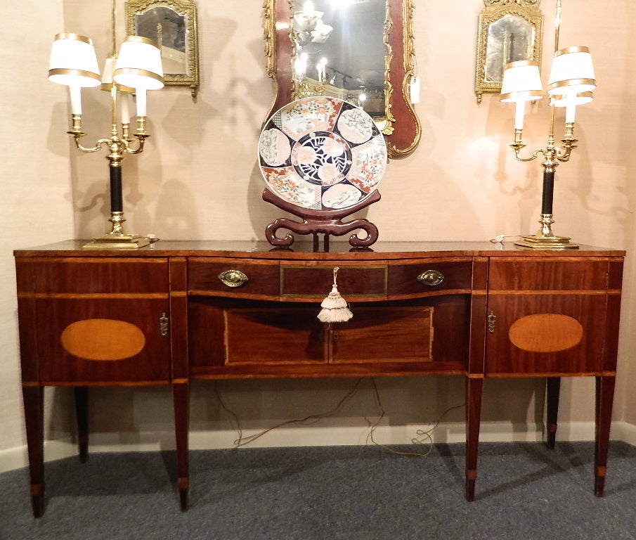 Late 18th Century Rare Size Regency sideboard with satinwood inlaid top and tapered spade legs.  The rectangular top banded and with a shaped front, above a conforming case fitted with a central cutlery drawer over a recessed cupboard, flanked to