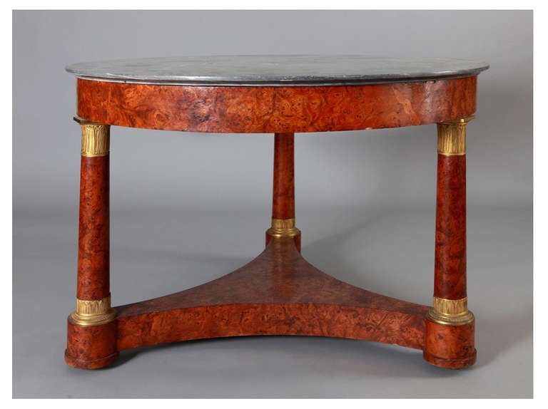 Guéridon in burlwood with marble top. The supports, which narrow from the base upwards, are mounted in gilt bronze whose design alludes to the base and capital of a classical column. The base of the guéridon is in the form of a solid triangle with