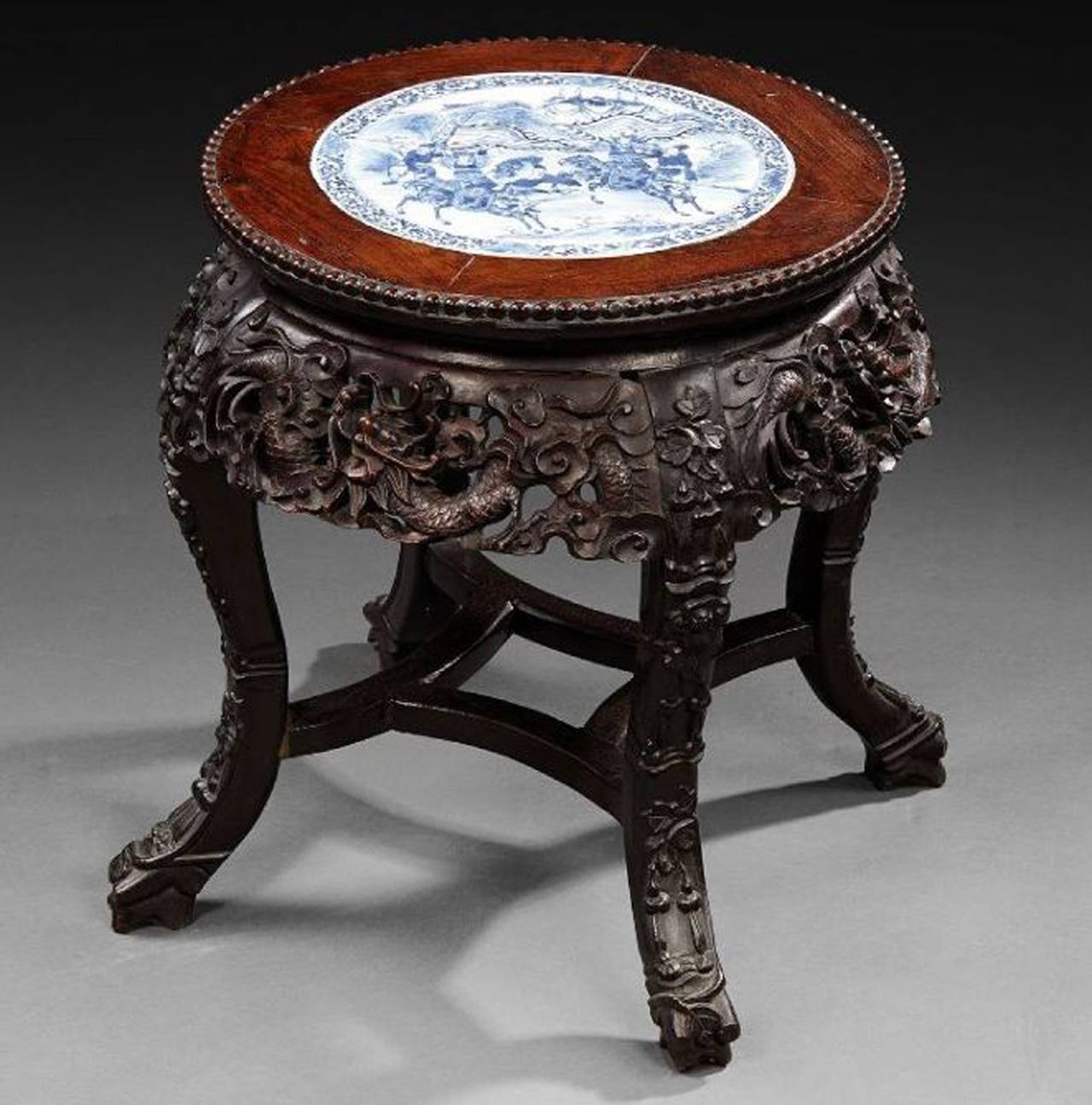 This dark wood stool is decorated with sculptures of dragons and plants.
It can be used as an occasional table.
 A blue and white porcelain plaque with a war subject is inlaid on the top of the table. 

Measures: High 45cm., diameter