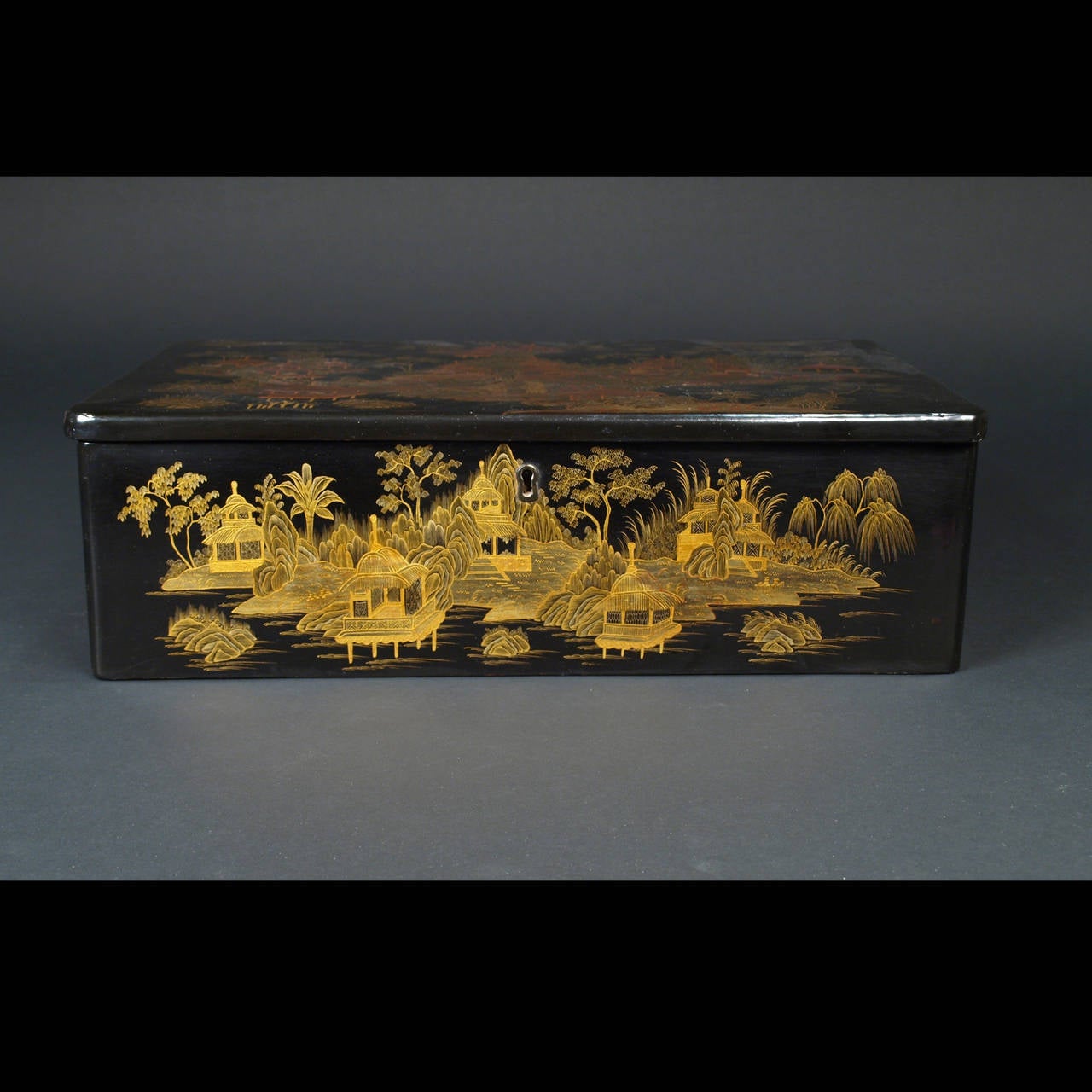 This Chinese export black and gilt lacquer box and cover, of oblong form is decorated in different tones of gold with landscapes showing buildings on foliage grounds, the interior has an inner tray with fitted compartments and various bone sewing