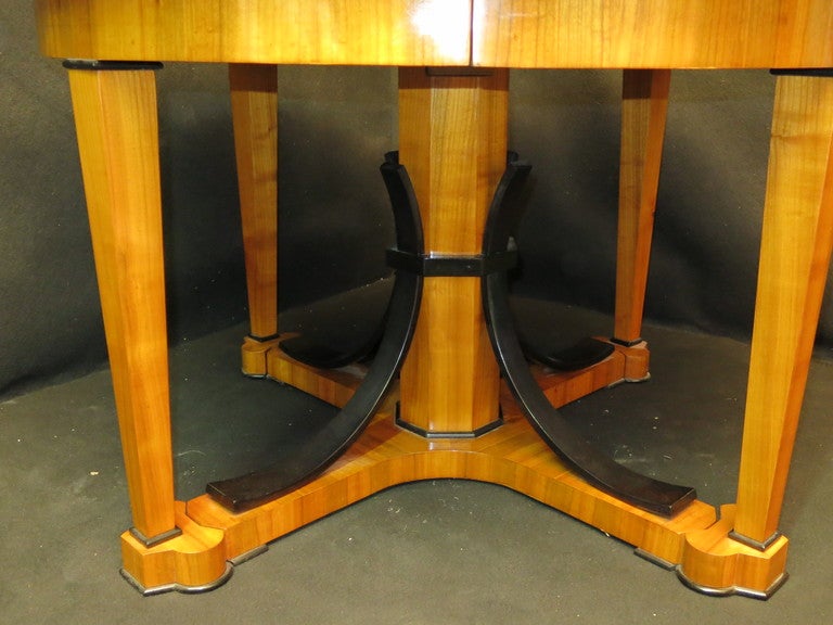 table in cherry veneered with details in black lacquer. the table open has 2 extensions veneered in cherry and 1 raw wood. the four legs come out and the central part remains stopped at the center. very stable.