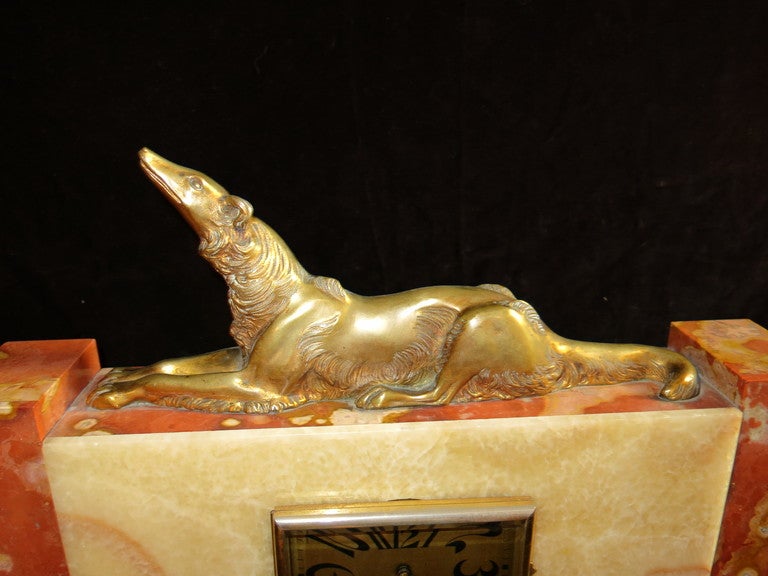 Classic fireplace clock, in red marble (diaspero di sicilia) and white onyx. Made up of three pieces, two rectangular side jars with brass feet and the central body containing the clock and with a fusion of a lying dog on it. The dial is very
