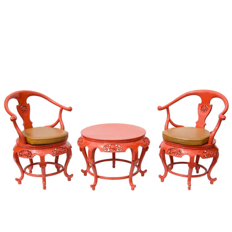 A small side table and two chairs in coral lacquer.