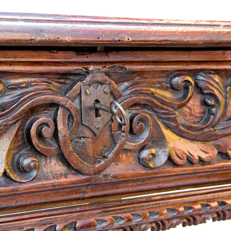A walnut table with the rectangular top above one ornately carved drop open panel with lock, concealing three smaller interior drawers raised on carved legs joined by a wood stretcher resting on scrolled carved feet.