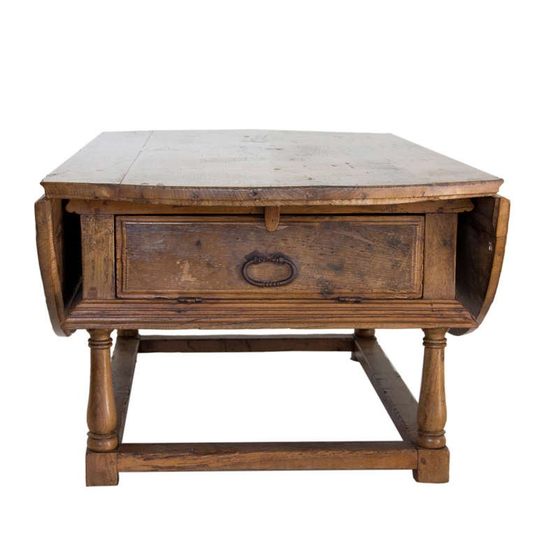 Catalan circular drop-leaf dining table with central drawers and supported by a wooden stretcher on turned legs.