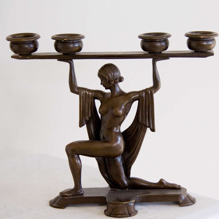 A bronze pair of candle holders depicting a womanin typical art deco clothing holding the candles