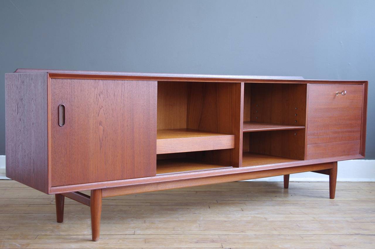 A low teak credenza designed by Arne Vodder for Sibast, circa 1960.

Includes five painted drawers that can be concealed with a sliding door. Sliding door reveals a pull-out shelf and drop-down door with lock reveals a cabinet ideal for bottle
