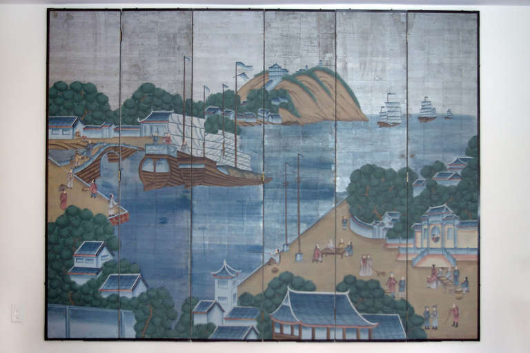 A large antique Chinese folding screen, consisting of six hand painted panels depicting a traditional harbor scene. Rendered mostly in shades of blue and green upon a silver background.  

An evocative and colorful piece.
