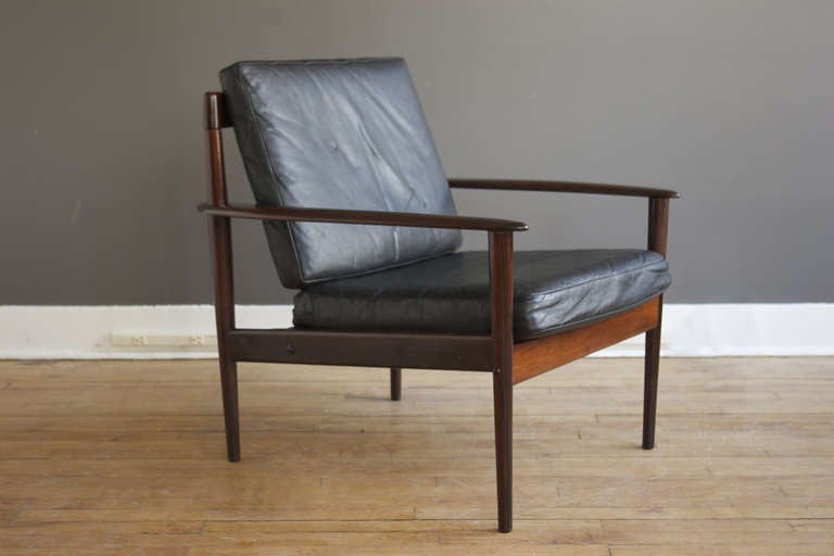 A classic lounge chair designed by Grete Jalk for P. Jeppesen, ca. 1956. Constructed of solid rosewood, with sculptural, flared arms and curved, bentwood back slats. Original black leather cushions are in good vintage condition. Retains Danish