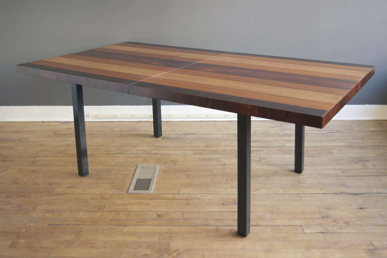 A beautiful and versatile dining table designed by Milo Baughman for Directional, ca. 1960. The top consisting of alternating stripes of richly grained rosewood, walnut and ash supported by a simple, rectilinear ebonized base with square legs.