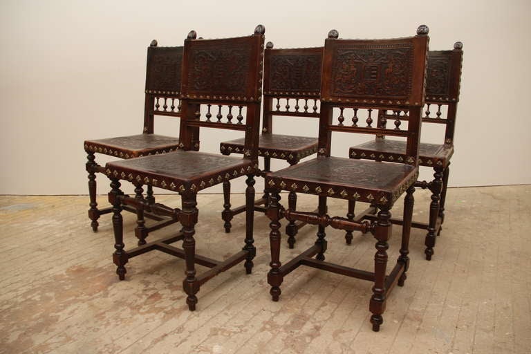 This set of 5 chairs are made of old growth walnut.  The seat and backs are made of embossed, hand-tooled leather secured with decorative, hand forged, scalloped brass tacks. The tooled leather depicts a floral design on the seat bottom and a scroll