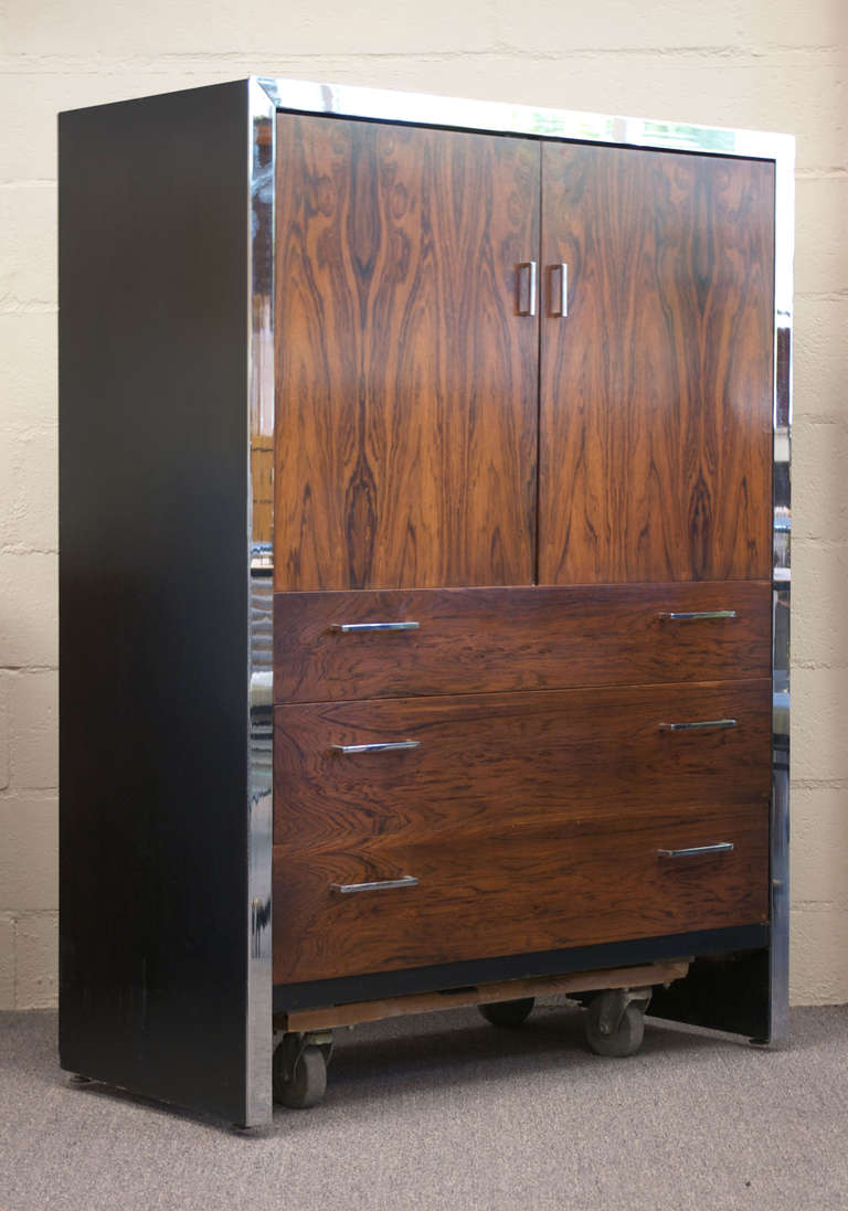 A tall black lacquer and rosewood dresser or wardrobe designed by Milo Baughman, possibly for John Stuart. Consists of an upper cabinet that opens to reveal a shelf and two drawers. Three deep drawers to bottom half. 

Chrome trim and hardware are