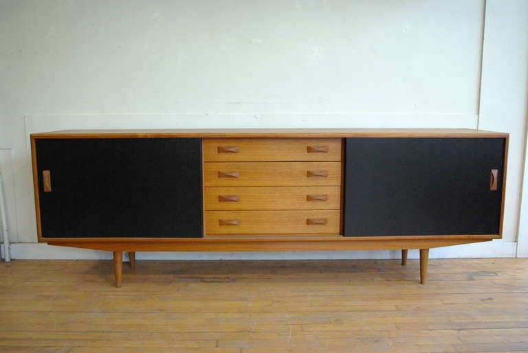 A long teak sideboard designed and manufactured by Clausen & Søn, ca. 1960s. Consists of two cupboards with sliding doors and interior shelves, in addition to a central bank of four, dovetailed drawers, each with carved bow-tie handles. The doors