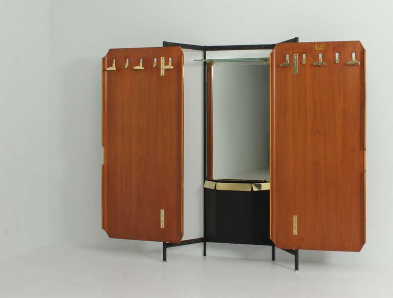 Nice entry wardrobe by La Permanente (Consorzio Esposizione Mobili Cantù), Italy, 1950s. Two rotary doors in plywood that hide a mirror, a shelf, one container and different hangers. Plywood, black lacquered metal, glass and brass.