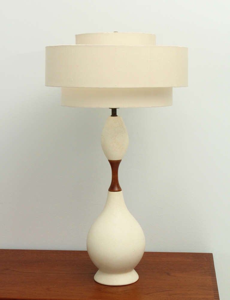 Large american mid-century ceramic table lamp from 1950's. Off white stucco ceramic base with teak wood and brass fittings and three parts shade with new fabric.