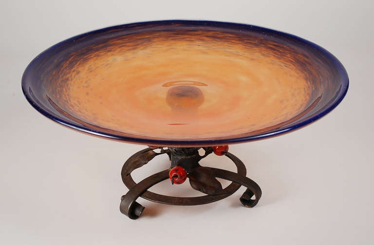Large French art glass compote by Charles Schneider. This compote has a wrought iron base with three glass berries attached. The glass bowl is orange with a blue rim.