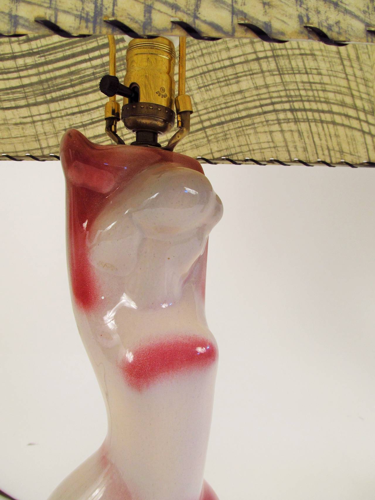 This lovely stylized female figure is attributed to The Heifetz Lamp Company, circa 1950s. The glaze is a soft oyster grey with a sort of raspberry pink accents. The shade is a period fiberglass rectangular shade in beige with grey brushstrokes.