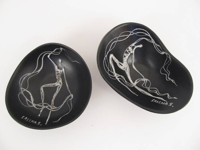 Stylized figures of women that appear to be made of smoke. The white linear decoration is textured on the surface in relief of the gloss black and gray field.  Very exotic and unusual Sascha Brastoff designs.

The smaller, rounder bowl is approx.