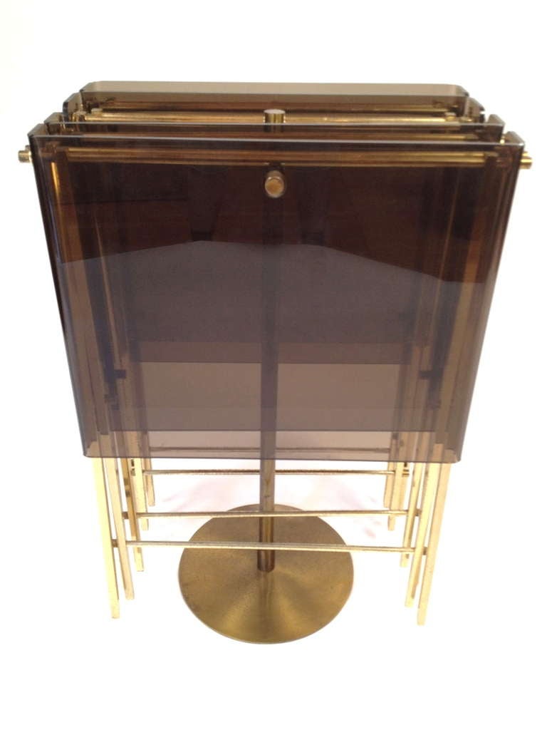 Set of 4 Charles Hollis Jones Brass and Smoked Lucite Folding Tray Serving Tables.  Tables hang on the stand when not in use.  Good original condition with a natural patina to the brass and some expected minor wear to the lucite surfaces from use as