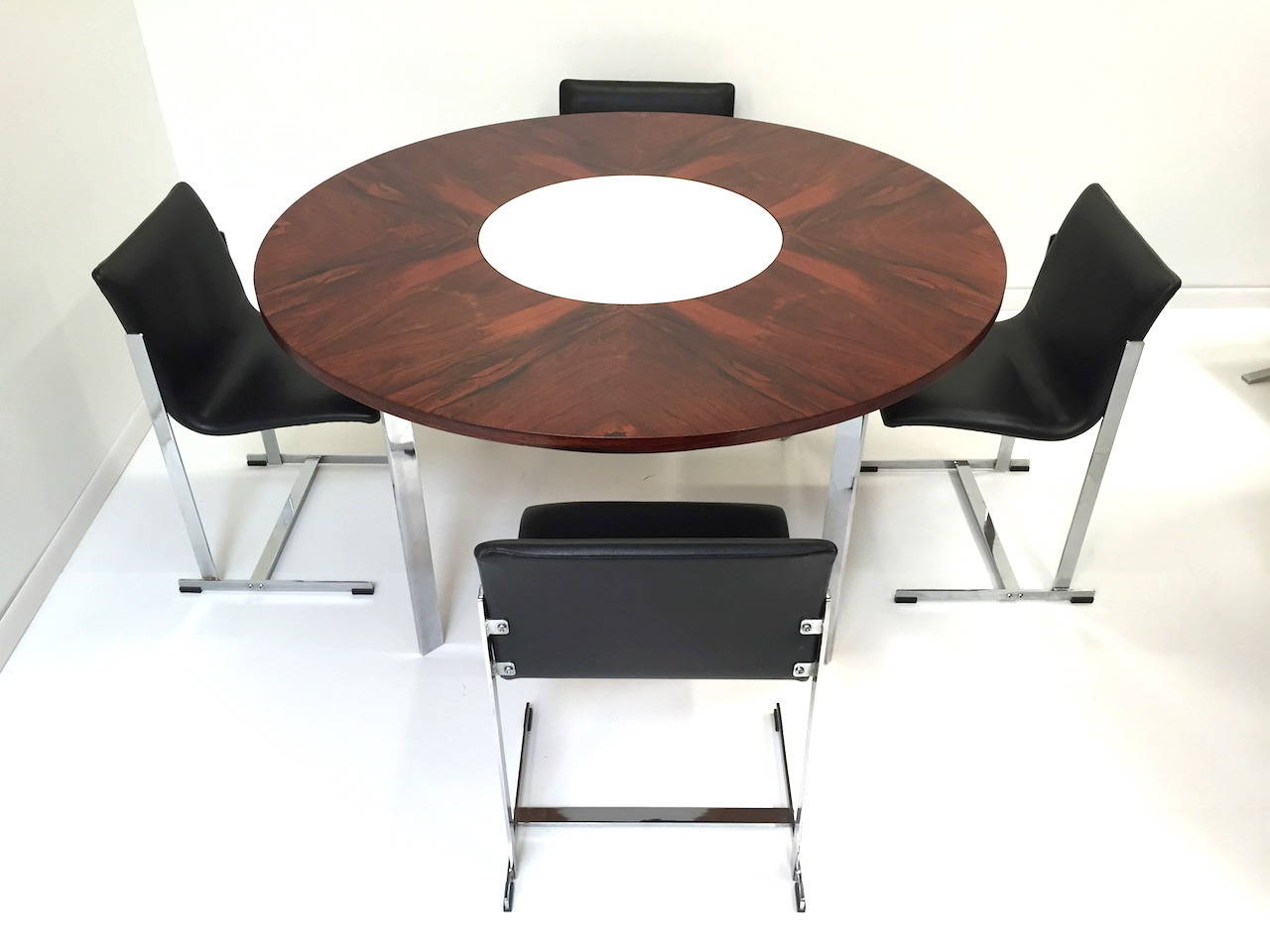 Merrow Associates rosewood Lazy Susan dining table and four cantilevered chrome chairs. Table features a revolving Lazy Susan Center and has been completely refinished including the white Formica center which was also replaced. Chrome has a minor