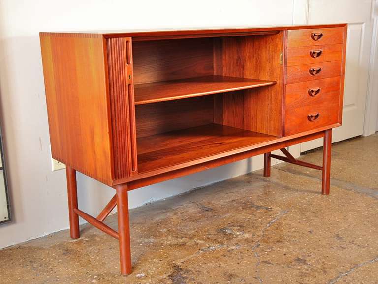 Exquisite sideboard designed by Peter Hvidt and Orla Mølgaard-Nielsen in 1956. This piece features a locking tambour door, four drawers (top drawer has felt and dividers), an adjustable shelf, and stunning exposed joinery. Long legs add to the