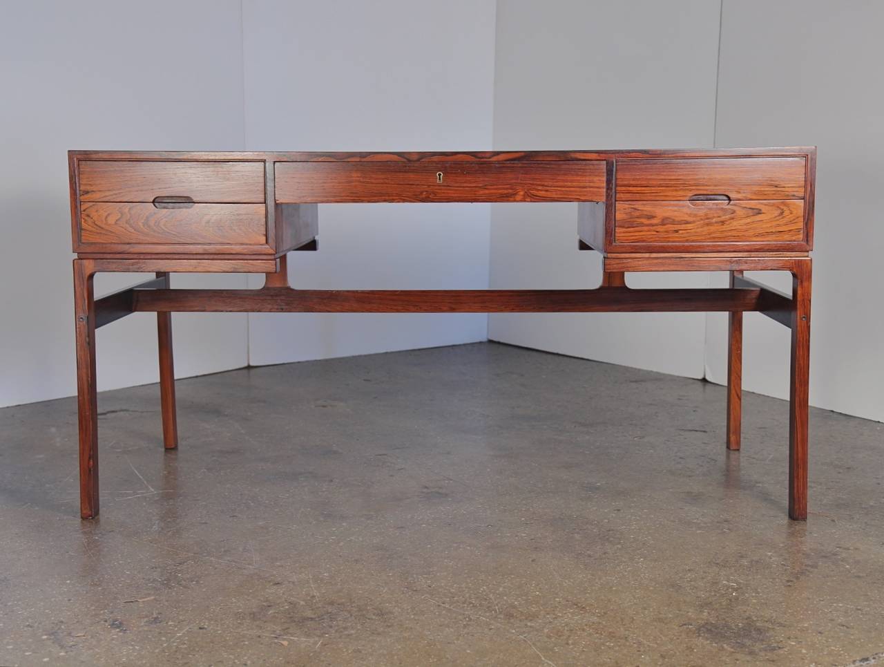 Elegant rosewood writing desk appears to float on a sculptural base. Highly figured rosewood desk top and exposed finger joints speak to the desk's exquisite craftsmanship. Five drawers with minimalist pulls. Finished in back with two generous