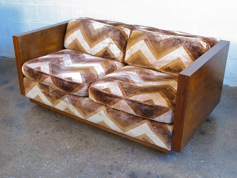 In the style of Milo Baughman: teak-framed love seat with high arms and finished back is upholstered in a decadent chevron-patterned velvet. Love seat sits on casters hidden under the teak base, which gives a floating effect. Couch is in excellent
