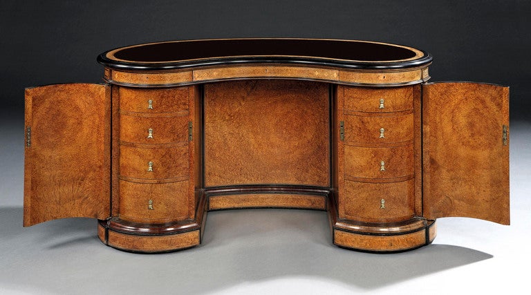 Constructed in thuyawood, with ebony stringing, and tulipwood cross banding; of kidney form, rising from a plinth base, having cupboard doors, each enclosing four interior drawers; three shaped drawers in the frieze, and with a tooled leather