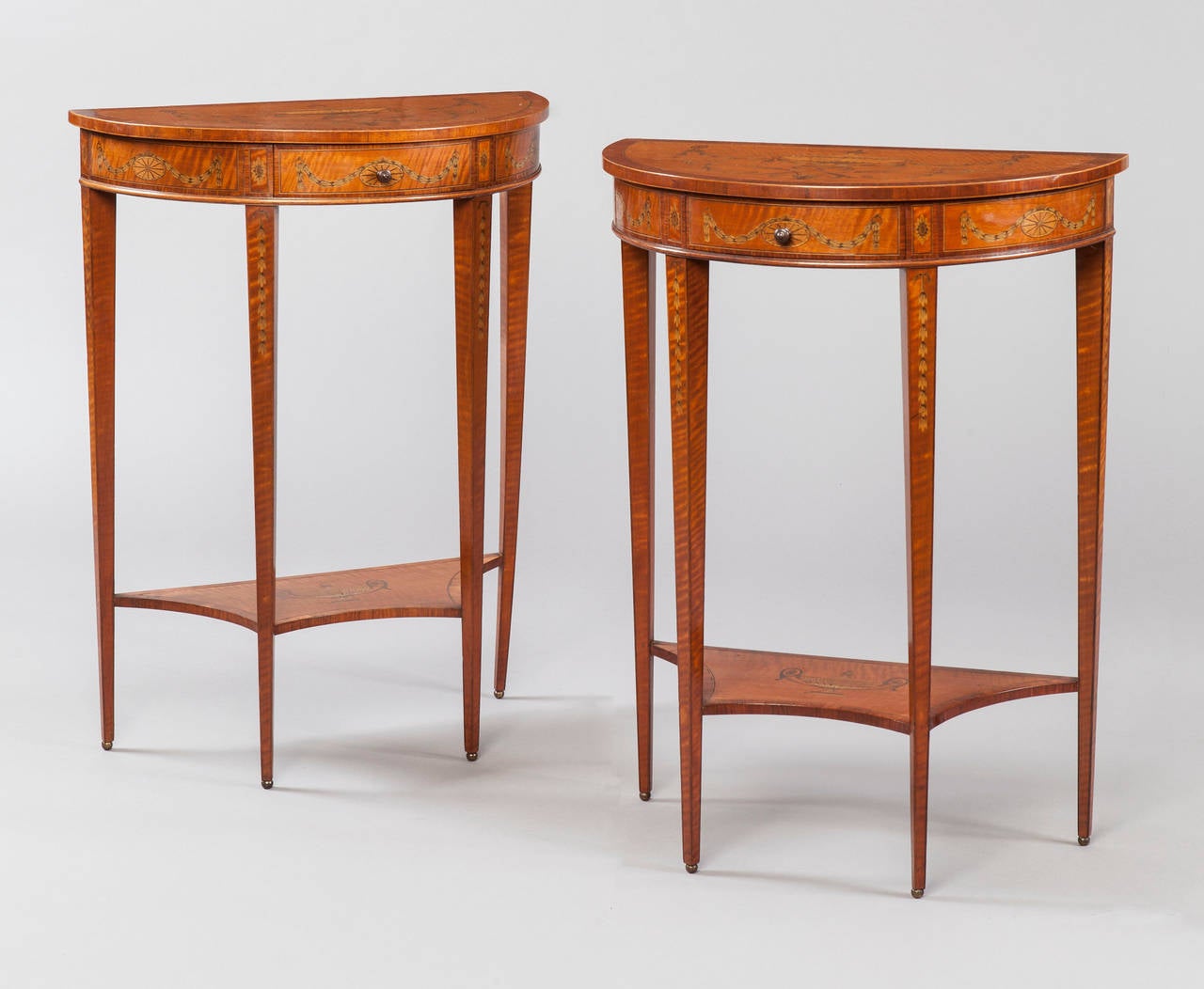A pair of console tables of diminutive size firmly attributed to Edwards and Roberts.

In the manner of Robert Adam, of demilune form, constructed in a well figured and grained West Indian satinwood, inlaid and cross banded; rising from tapering
