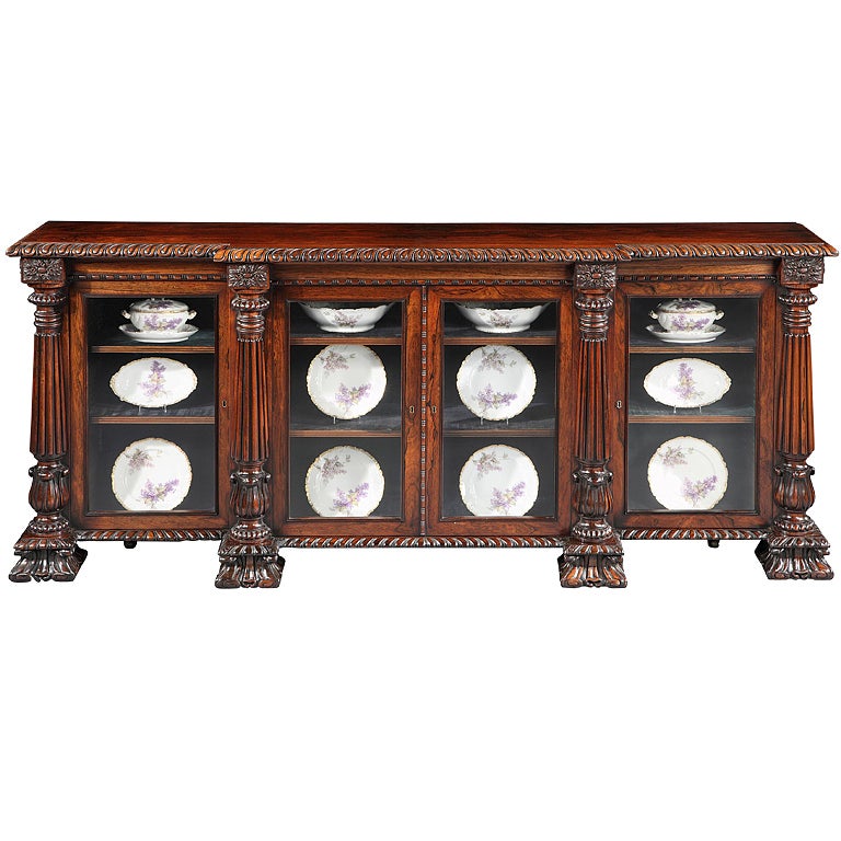 Constructed of finely figured rosewood, of four door breakfront form, exuberantly carved in the Graeco-Roman taste, rising from acanthus carved splay feet: the lockable glazed doors housing adjustable shelves, and framed within tapering, lobed and