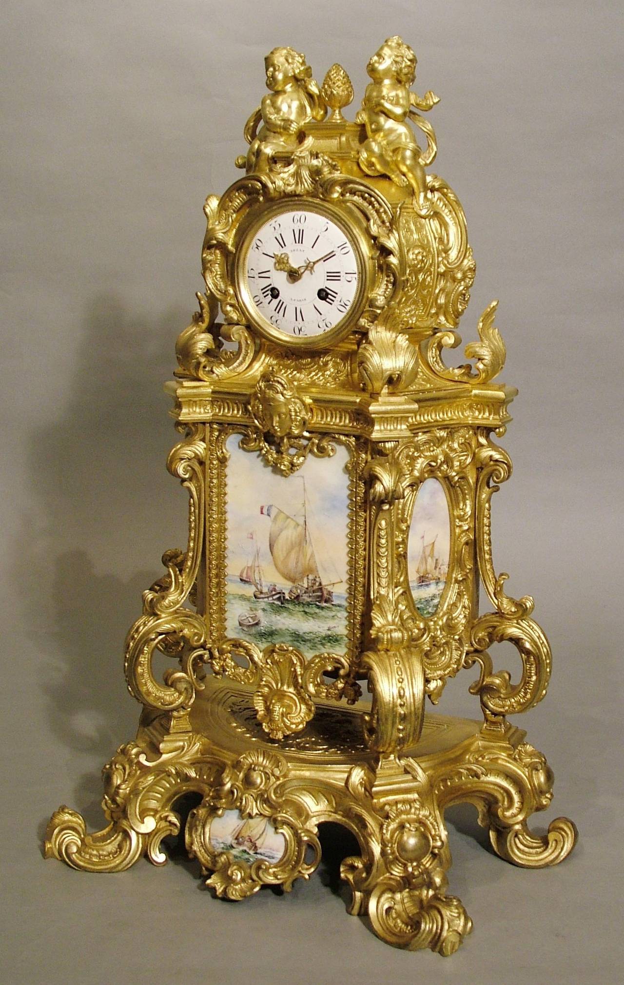 An impressive French mantel clock by LeCat of Paris.

Constructed in the Louis XV manner, the monumental gilt bronze framework housing hand-painted porcelain plaques of nautical scenes, signed ‘Venoit; rising from scrolled feet, the exuberantly