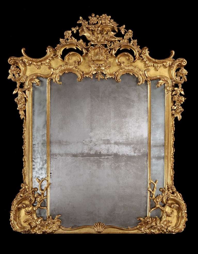 The mirror frame of serpentine symmetrical shape, being gilded; decorated with exuberant ‘C’ scrolls, naturalistic trees, foliates, and having two turtle doves atop; the triple mercury backed mirror plates divided by decorated vertical spacers.