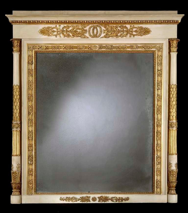 Of rectangular form, the frame housing the mirror plate finished in ivory paintwork, with gilt and burnished gilt highlights; the everted cornice decorated with egg and dart mouldings, with a pediment above; the flanking shaped columns dressed with