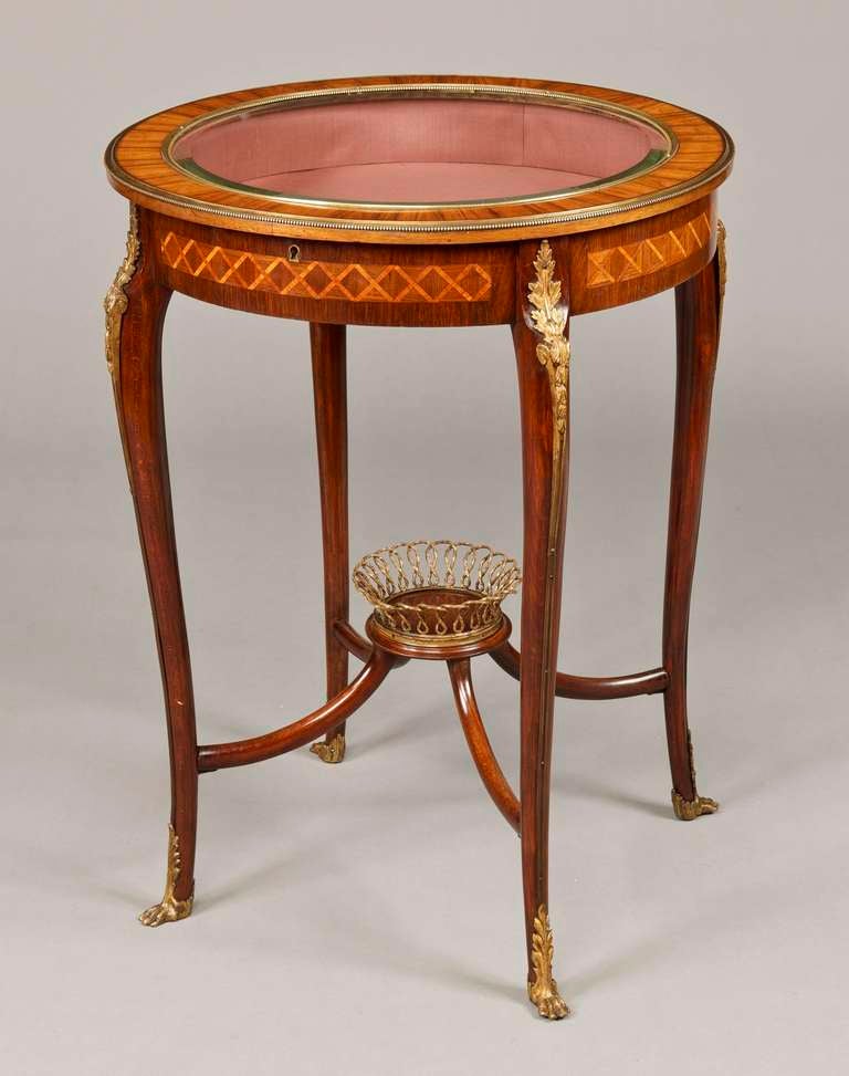Constructed in rosewood, with parquetry inlays in tulipwood and kingwood; rising from gilt bronze sabot shod feet, the swept cabriole legs having four upwardly swept stretchers supporting a wirework basket of arcaded form; the circular display
