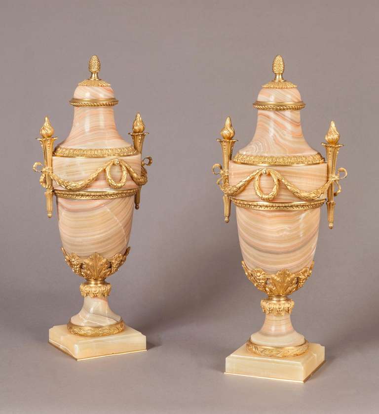 A Good Pair of Antique French Urns in the Louis XVI Taste

Constructed in Algerian Rose Onyx, dressed with Bronze ormolu mounts: rising from square bronze mounted bases, the baluster form urns have ormolu flambeaux handles, conjoined with swagged