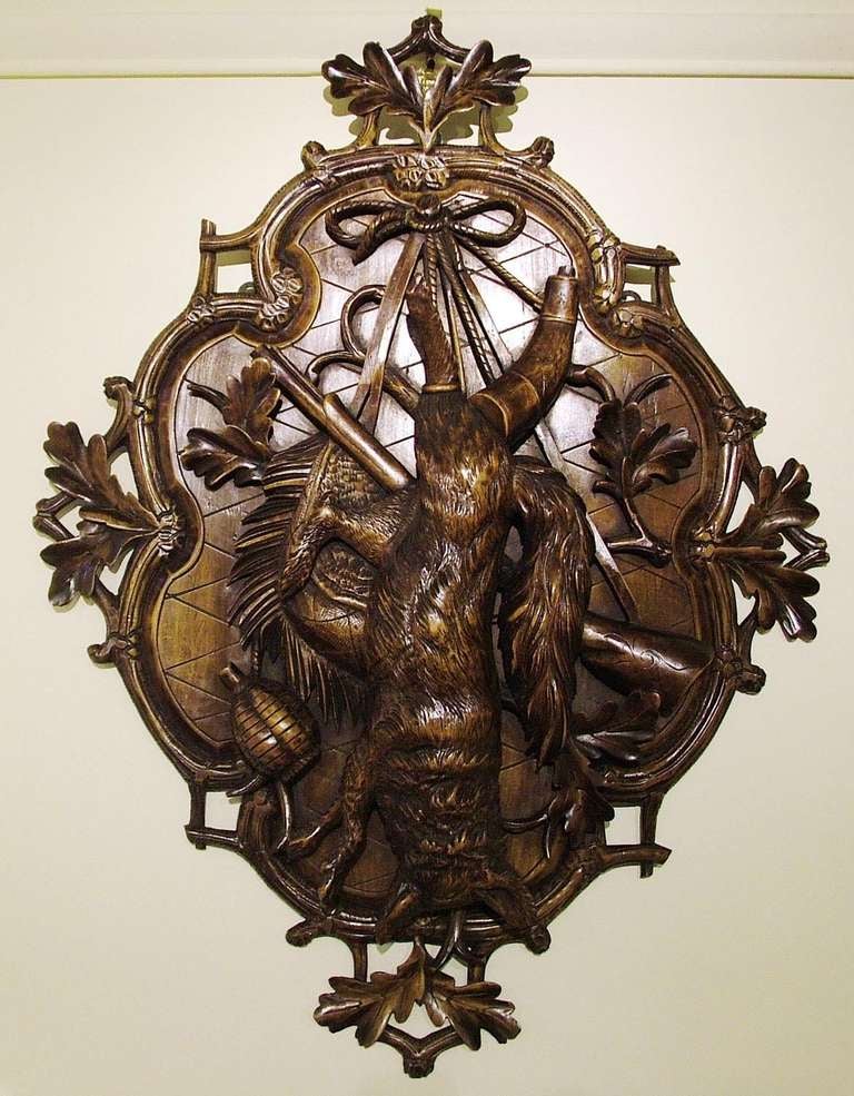 A well executed hand-carved limewood piece of asymmetrical form, centred around a pendant fox, which has glass eyes, powder flasks and a hunting rifle and pouch backing; a plaited rope atop; the frame profusely carved with foliage. 

Literature: