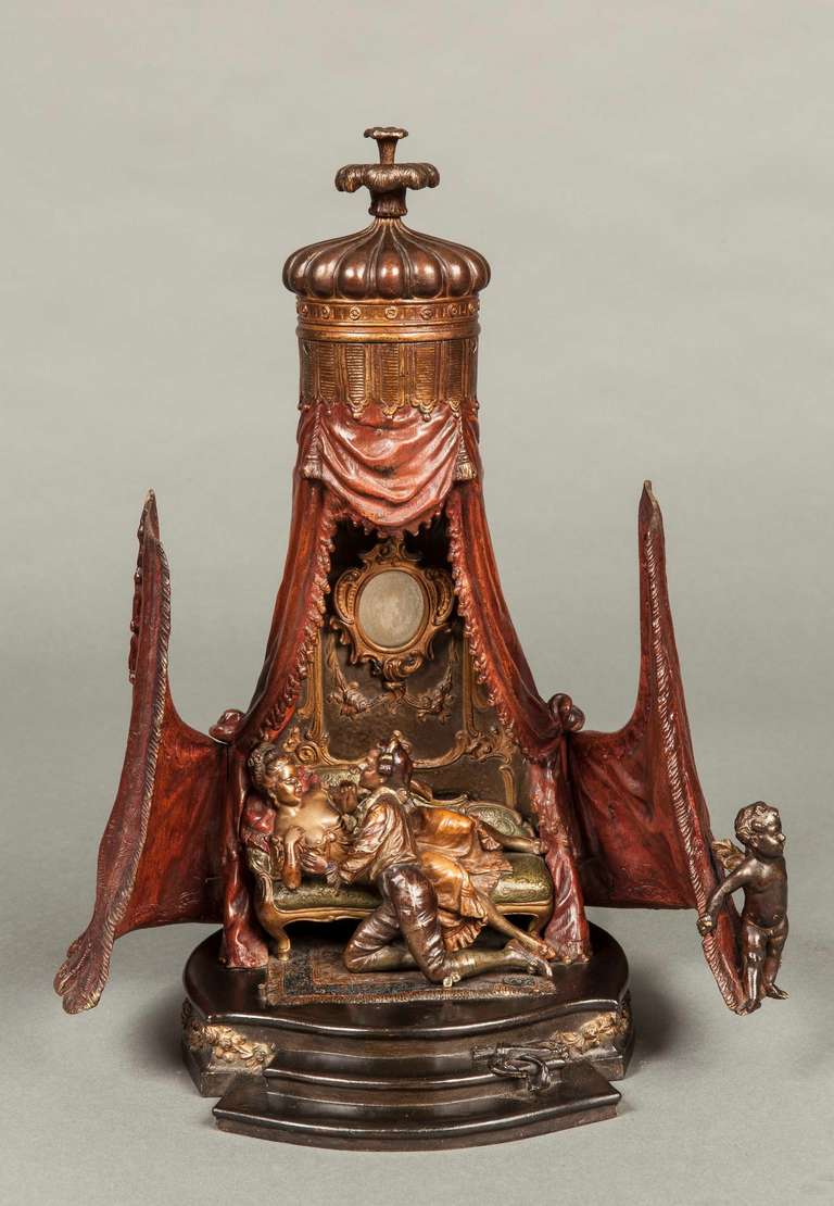 The cold painted bronze depicting a closed tent, has button released double doors, one with a smirking cupid, opening to reveal a young blood ardently courting a not unwilling de´shabille´ female comfortably draped on a chaise longue, set in a room