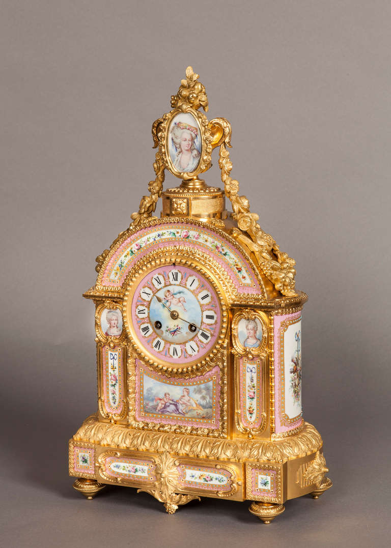 Constructed in a fine quality two-tone ormolu case, and adorned with rose ground ‘Sevres’ style panels to both front and sides, depicting; rising from oblate toupie feet, the domed case is of modest breakfront form, with a flambeaux urn atop, having