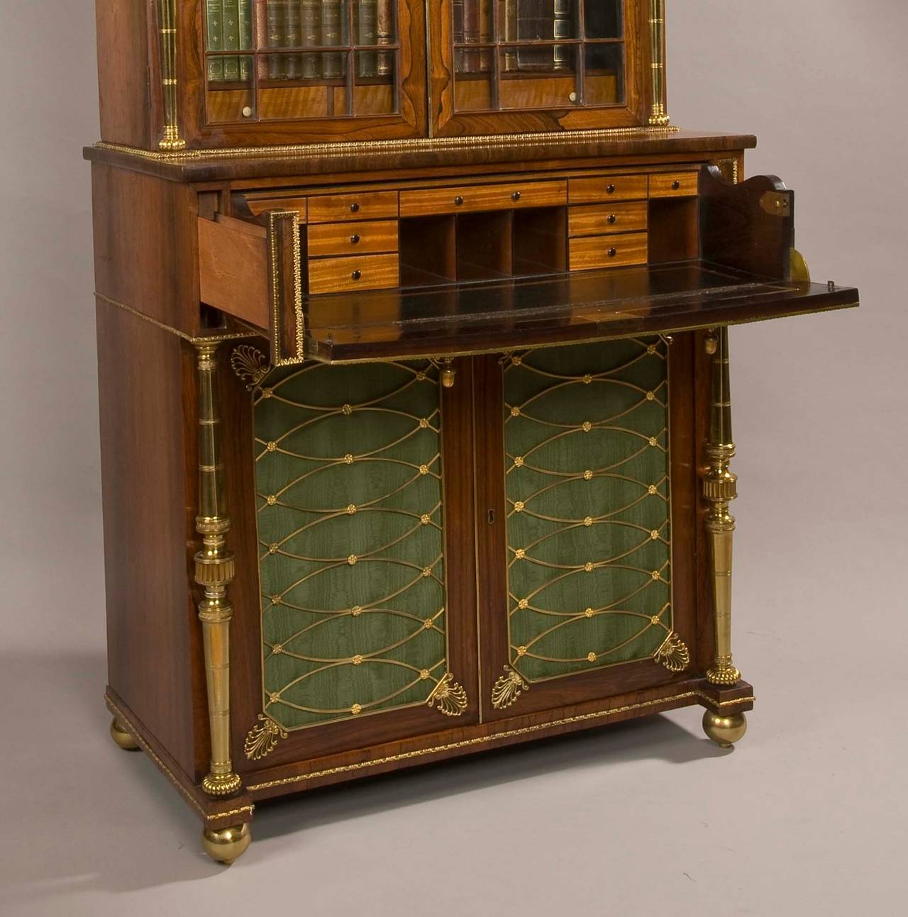 A Regency period secretaire bookcase attributed to John Mclean of London.

Constructed in a well figured goncalo alves, with extensive use of gilt brass accents. Rising from compressed ball brass feet, the lower section consists of two blind