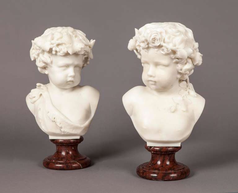 Carved in white Carrara marble, the busts, emblematic of Summer and Autumn, are supported on circular stepped & tapering Rouge Griotte pedestals; the male putti, representing Autumn, is draped with vines and ripened grapes, and the female child,