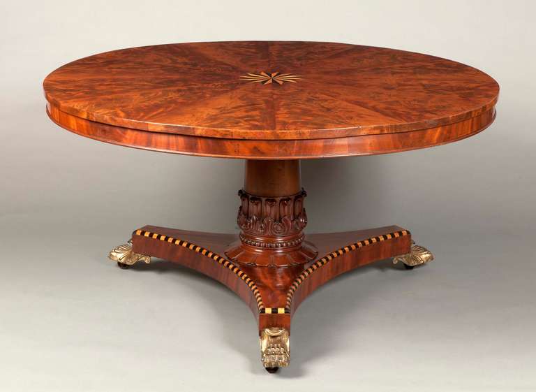 Constructed in Cuban mahogany, with holly and bois Clair inlays; the circular tilt top having radially laid flame Mahogany veneers of magnificent figuring and colour, with a ‘starburst’ inlay to the centre; supported by a turned and tapering column,