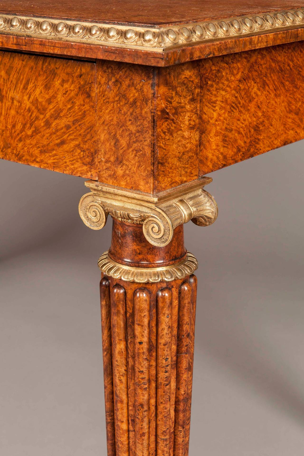 A library table of the Regency period In the Manner of Marsh & Tatham

Of rectangular form, constructed using amboyna, with ormolu accents; rising from ring turned and tapering lobed legs, with ormolu stiff leaf collared feet and shoulders,