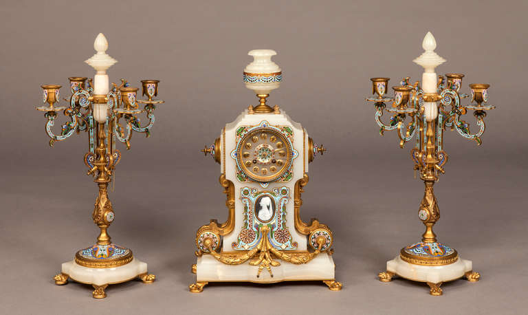 A French Clock Garniture of the Napoleon III Period By ‘La Compagnie des Marbres et Onyx d’Algerie’

Constructed in onyx, gilt bronze and decorated with champlevé enamel, and comprising the clock, and matching candelabra; the clock, of