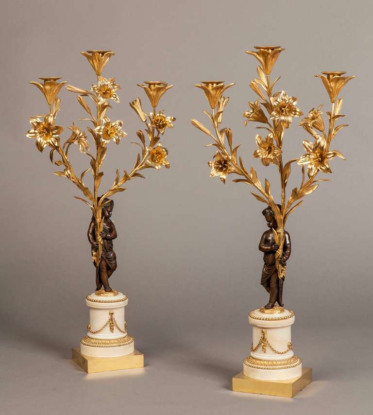 A Fine Pair of Candelabra of the Louis XVI Period

Constructed in gilt bronze and white Cararra marble; rising from square gilt bronze bases, the drum form marble columns being draped with bronze chains and festoons; the patinated bronze putti