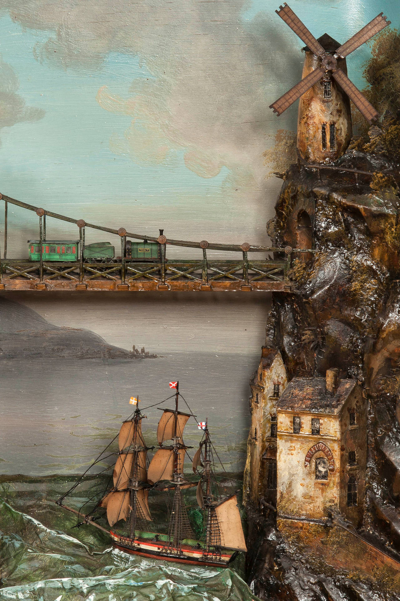 Housed within a swept gilt rectangular frame, the mountain and lake hand painted diorama incorporates a rolling ship, bearing the white saltire on red flag of St. Patrick, a train, a windmill, a water wheel, a horse and cart, inter alia, as well a