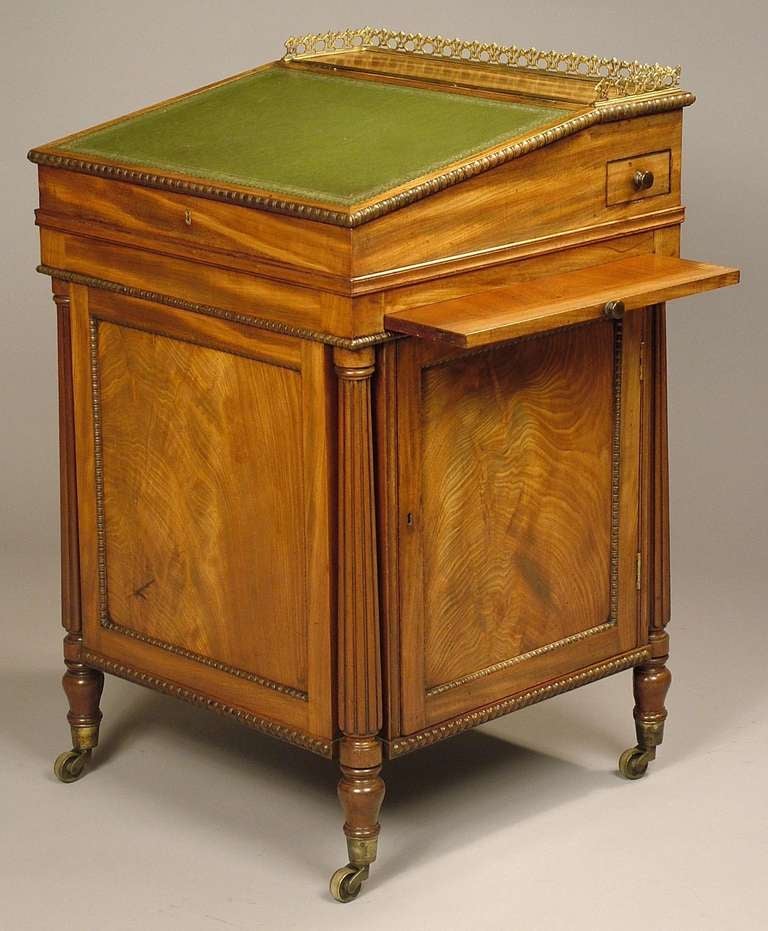 Constructed in mahogany, rising from castor shod turned feet, the base of square form, having reeded columns to the angles, and a lockable side door enclosing four graduated drawers with brass knobs; the writing slope of sliding form, flanked by