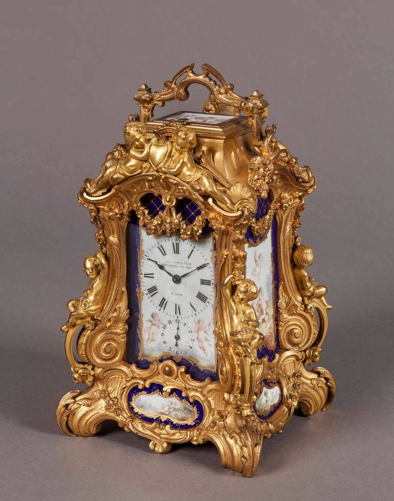 An ornate carriage clock in the manner of Alfred Drocourt of Paris 

The ornate gilt brass case, rising from swept feet having serpentine angles dressed with cast and chased spandrels and putti, the swaged frames housing the gros bleu and giltwork