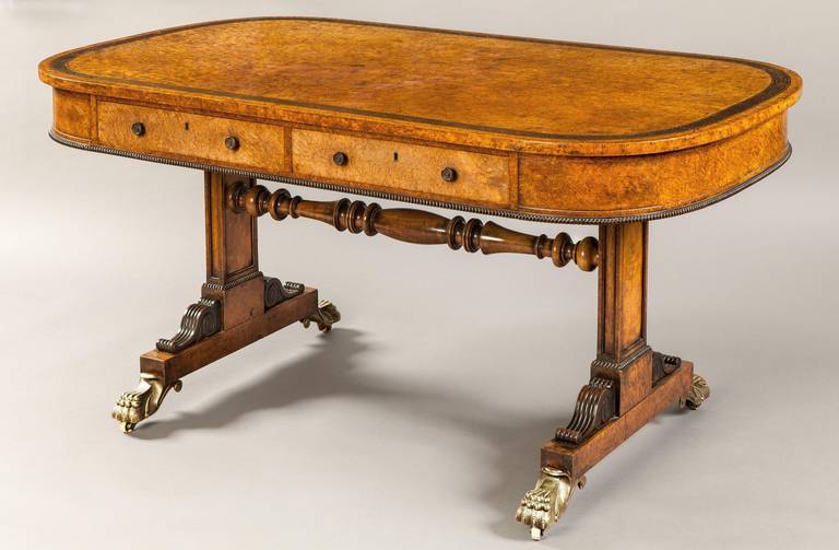 A library table in the manner of Gillows 

Constructed in amboyna, with cut gold brass inlay work, and bronze feet; of rectangular panelled end support form, braced by pairs of carved spandrels, rising from porcelain caster shod swept talon feet,