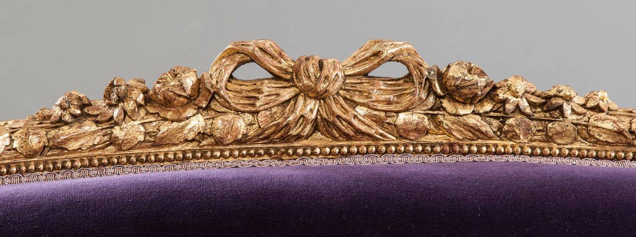 A grand Canapé in the Louis XVI manner.

Constructed in a well carved gold giltwood, with later purple velvet upholstery; rising from turned and tapering legs with toupie feet, the shaped front rails embellished with carved running Bellflower
